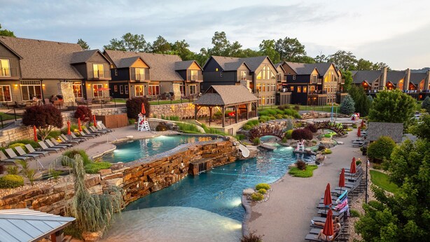 Un resort con piscina, sillas de descanso y un puente de piedra.