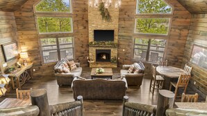 Interior acogedor de una cabaña de madera con chimenea, muebles de madera y grandes ventanas que ofrecen vistas del exterior.