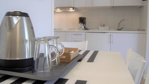 Une cuisine moderne avec des meubles blancs, une bouilloire en acier inoxydable et un plateau sur lequel se trouvent une tasse en verre et une boîte en bois.