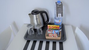 Un plateau avec une cafetière Philips, deux verres, un carton de jus Vimeiro et une boîte de collations Delta, le tout posé sur une table blanche.