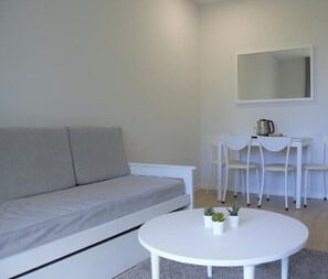 Een moderne woonkamer met een grijze bank, een witte salontafel met planten en een witte eethoek met stoelen.