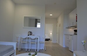 Een moderne, minimalistische leefruimte met een eethoek, kitchenette en een slaapkamer op de achtergrond.