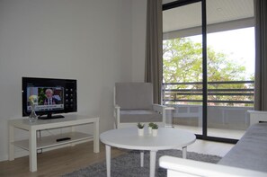 Een moderne woonkamer met een televisie, een witte salontafel, een grijze fauteuil en een bank.