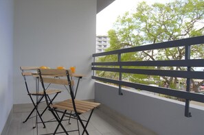 Un balcón con barandilla de metal, una mesa de madera y dos sillas.