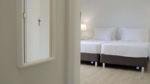 Une chambre avec deux lits, une porte et une table de chevet avec une lampe.