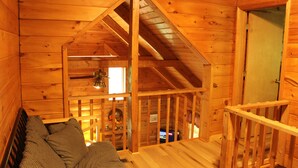 A wooden cabin interior with a loft bedroom, a wooden staircase, and a cozy seating area. - Our open 2 -story, 2- Bedroom Cabin! (Hico)