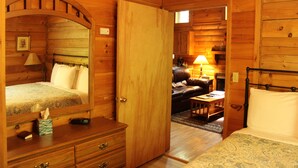 A wooden cabin room with a bed, dresser, and a small table. - Our open 2 -story, 2- Bedroom Cabin! (Hico)