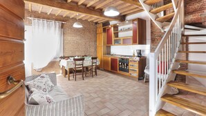 A rustic kitchen with exposed brick walls, wooden beams, and a white staircase.