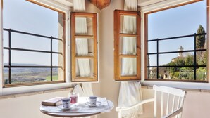 A corner room with two windows, a table with a book and cups, and a chair.