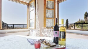A table with wine bottles and glasses, a fruit drink, and almonds on a balcony with a scenic view.