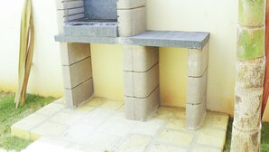 Una parrilla de concreto con superficie plana y chimenea, frente a una pared amarilla.