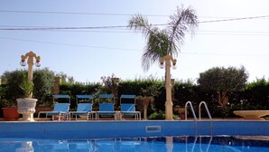 Una piscina con azulejos azules, rodeada de sillas de descanso y plantas en macetas.