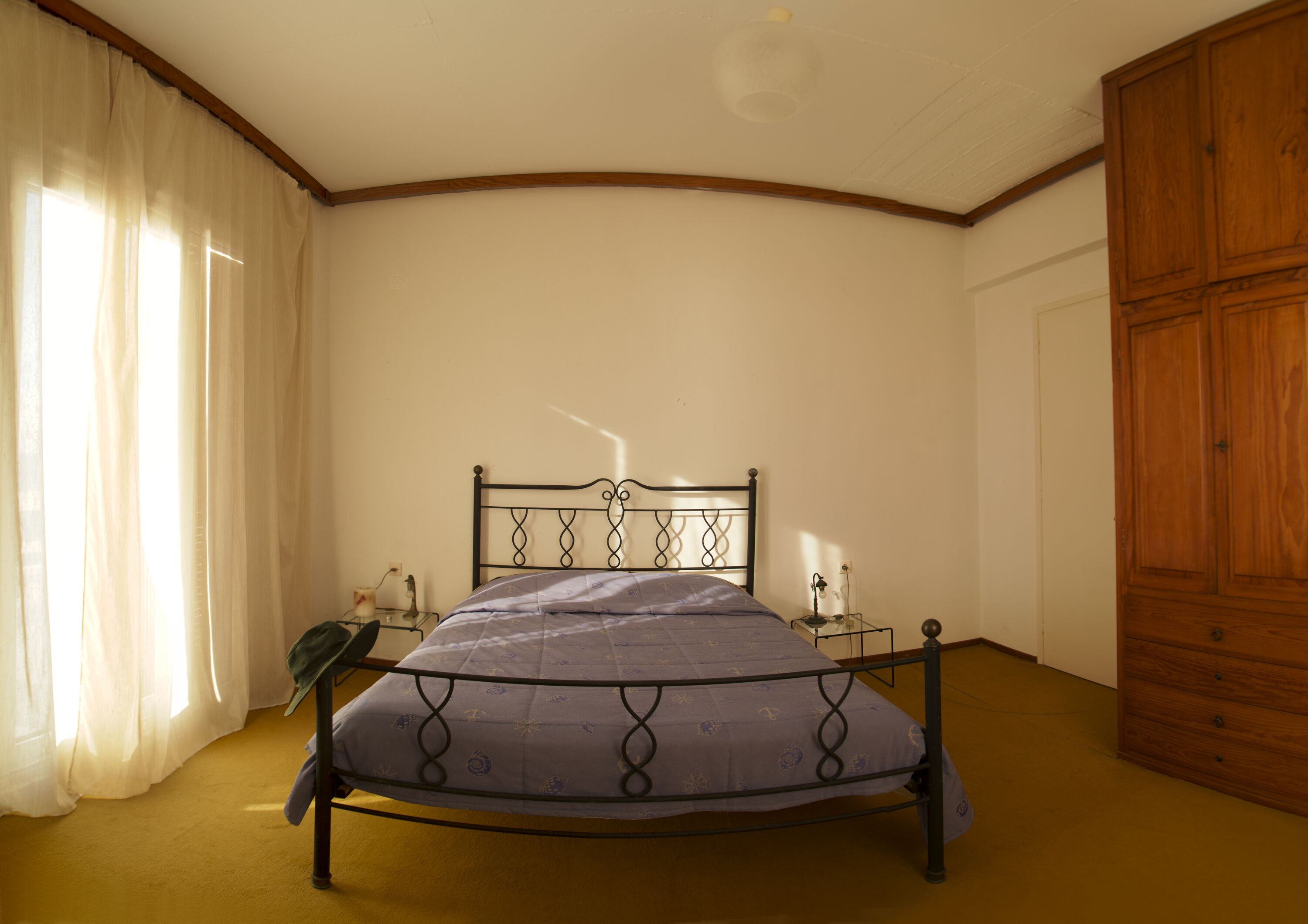 A bedroom with a bed, a nightstand, a lamp, a wardrobe, and a window with curtains.