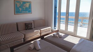 A hotel room with a large window offering a view of the sea, a striped sofa, two beds with towels, and a world map on the wall. - Villa Moby Dick – Beachfront Stay on the Ionian Sea (preveza)