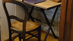 A wooden chair with a woven seat, a small table with a purple notebook, a lamp, and a stone wall.