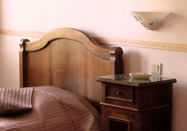 A bedroom with a wooden headboard, a bed with a pillow, a nightstand with a lamp, and a wall-mounted light fixture. - Charming room LES VIGNES (Andilly)
