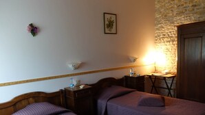 A room with two beds, a small table with a lamp, a water bottle, and a framed picture on the wall.