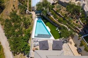 Vue aérienne d’un espace piscine moderne, avec une piscine rectangulaire entourée de murs en pierre et de verdure.