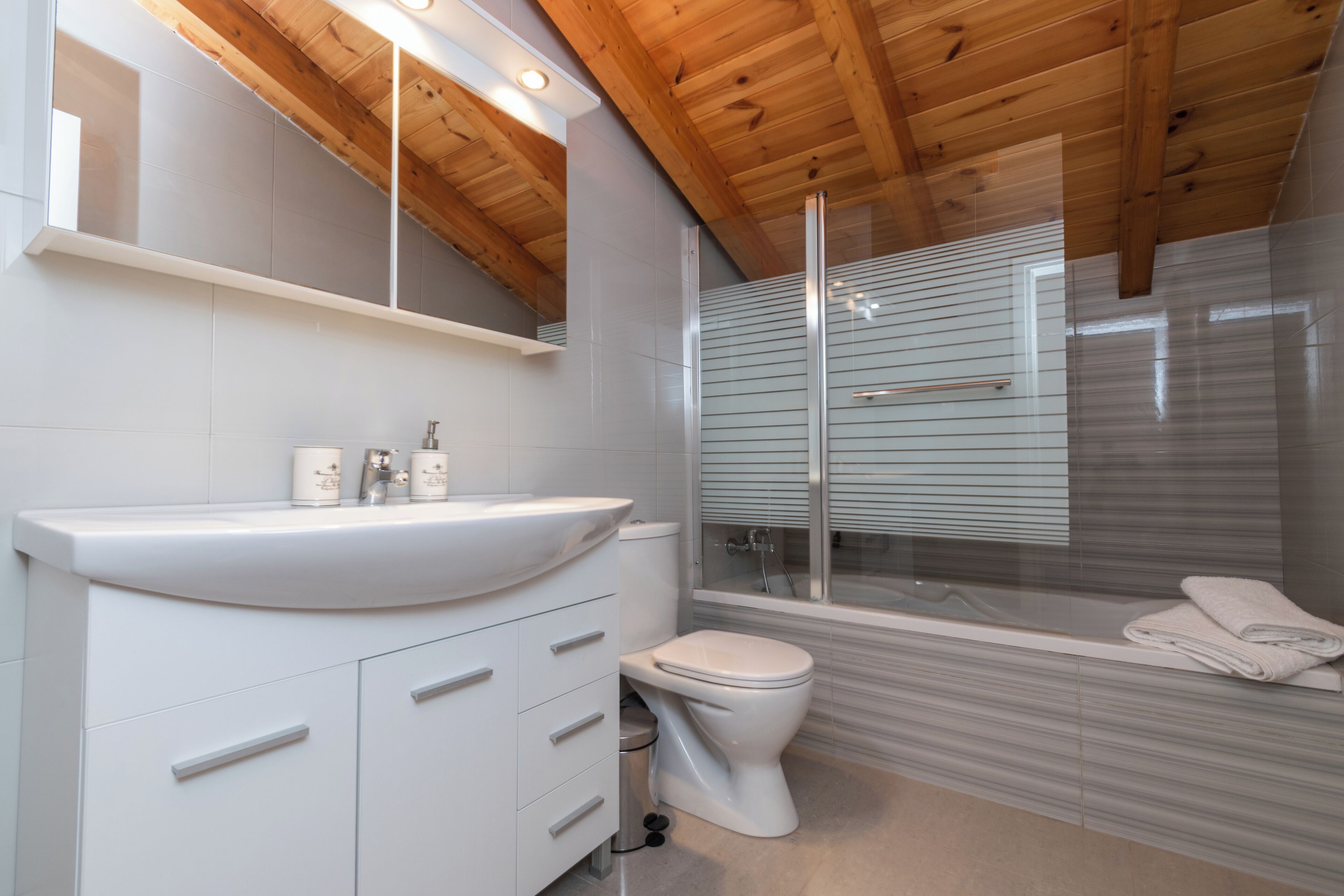 Une salle de bain moderne avec un plafond en bois, un lavabo blanc et une douche à parois de verre.
