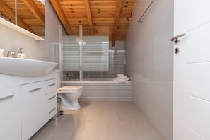 Une salle de bain moderne avec un plafond en bois, un lavabo blanc, des toilettes et une douche en verre.