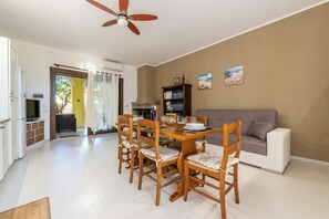 A dining area with a wooden table and chairs, a ceiling fan, and a gray sofa. - Villa Veronica Villasimius code IUN P5506 (Villasimius)