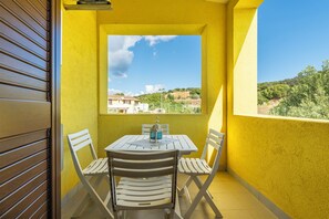 A balcony with a yellow wall, a table with chairs, and a view of a green landscape. - Villa Veronica Villasimius code IUN P5506 (Villasimius)