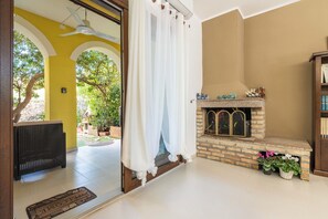 A room with a fireplace, a wicker sofa, and a view of greenery outside.