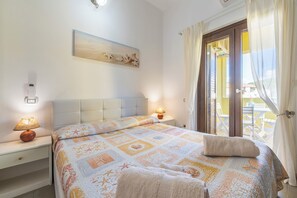 A bedroom with a bed, bedside lamps, a wall clock, and a view of the outside balcony. - Villa Veronica Villasimius code IUN P5506 (Villasimius)