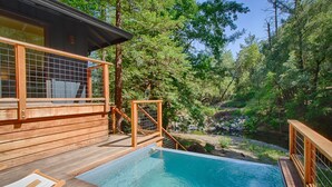 Une terrasse en bois avec une piscine, entourée d’arbres et d’un paysage naturel.