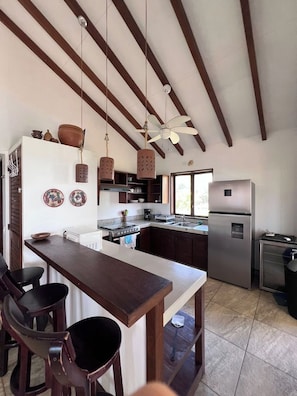 A kitchen with a central island, wooden ceiling beams, hanging pendant lights, and a refrigerator. - Relax in Style – 2BR Beachfront with Pool at Playa Tesoro (Salines Grandes)