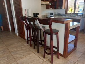 Uma cozinha com ilha central, banquetas, micro-ondas e dispensador de água.