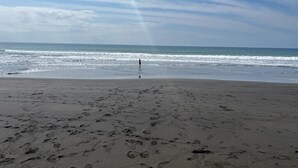 Una playa con huellas que conducen al agua, una persona de pie a lo lejos y un cielo despejado.