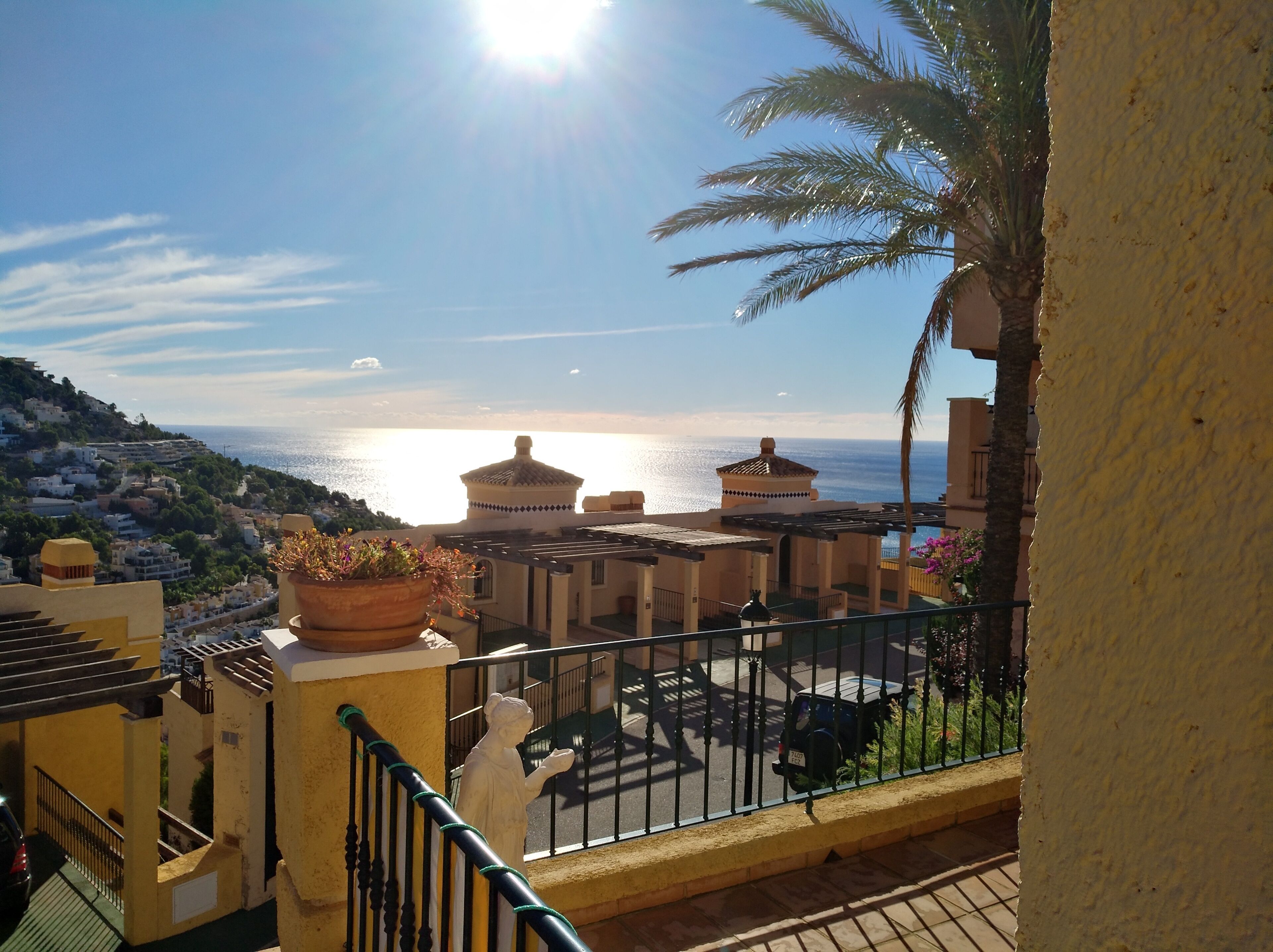 A terrace with a view of the sea, a statue, and a building with a dome.