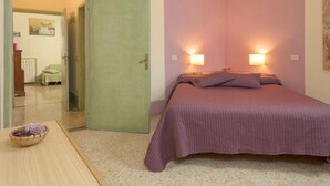 A bedroom with a bed, two bedside lamps, a door, and a small table with a basket. - Edera cozy house in Tuscan village (Castel San Gimignano)