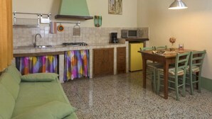 A compact kitchen with a dining area, a green sofa, and a small table with chairs. - Edera cozy house in Tuscan village (Castel San Gimignano)