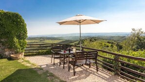 An outdoor seating area with a table and chairs, a wooden fence, and a view of rolling hills. - Edera cozy house in Tuscan village (Castel San Gimignano)