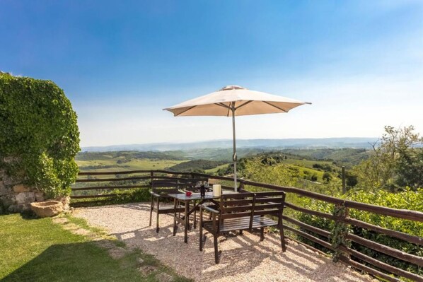 An outdoor seating area with a table and chairs, a wooden fence, and a view of rolling hills.