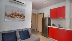 Eine moderne Küche mit roten Schränken, einem Edelstahlkühlschrank und einem grauen Sofa mit blauen Kissen.