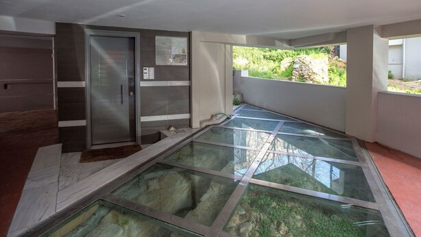 Ein modernes Interieur mit gläsernem Boden, der zu einem Balkon führt, einer Schiebetür und Blick auf Grünflächen.