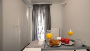 Ein Hotelzimmer mit Bett, Frühstückswagen mit Croissants, Äpfeln, Orangensaft und einer Kaffeetasse.