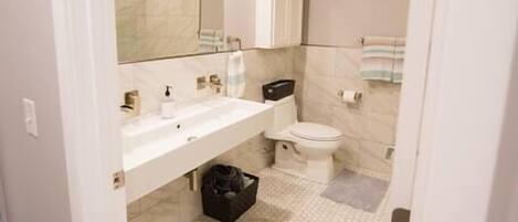 Um banheiro moderno com toucador branco, um espelho grande, vaso sanitário e piso com padrão hexagonal.