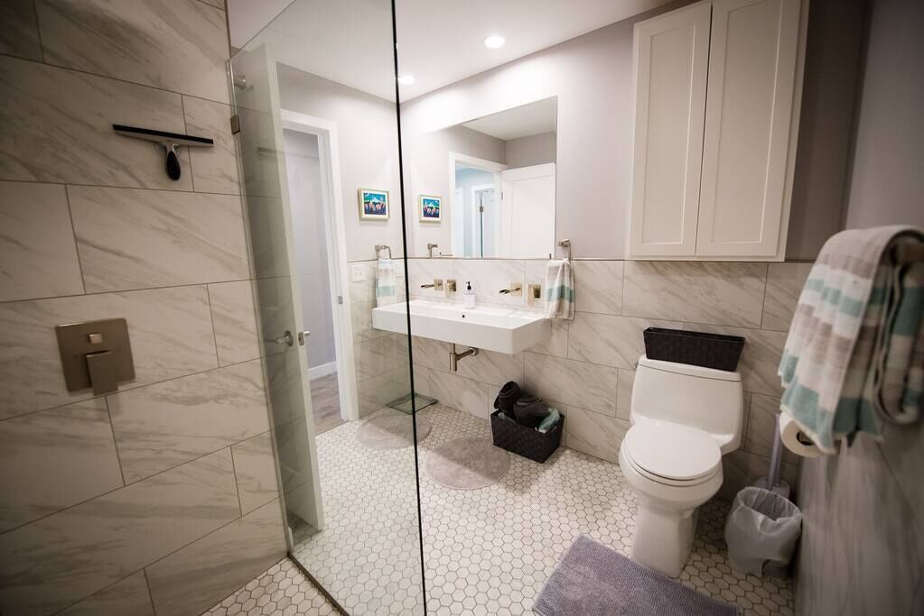 Un baño moderno con cabina de ducha de vidrio, un lavabo blanco, inodoro y espejo.