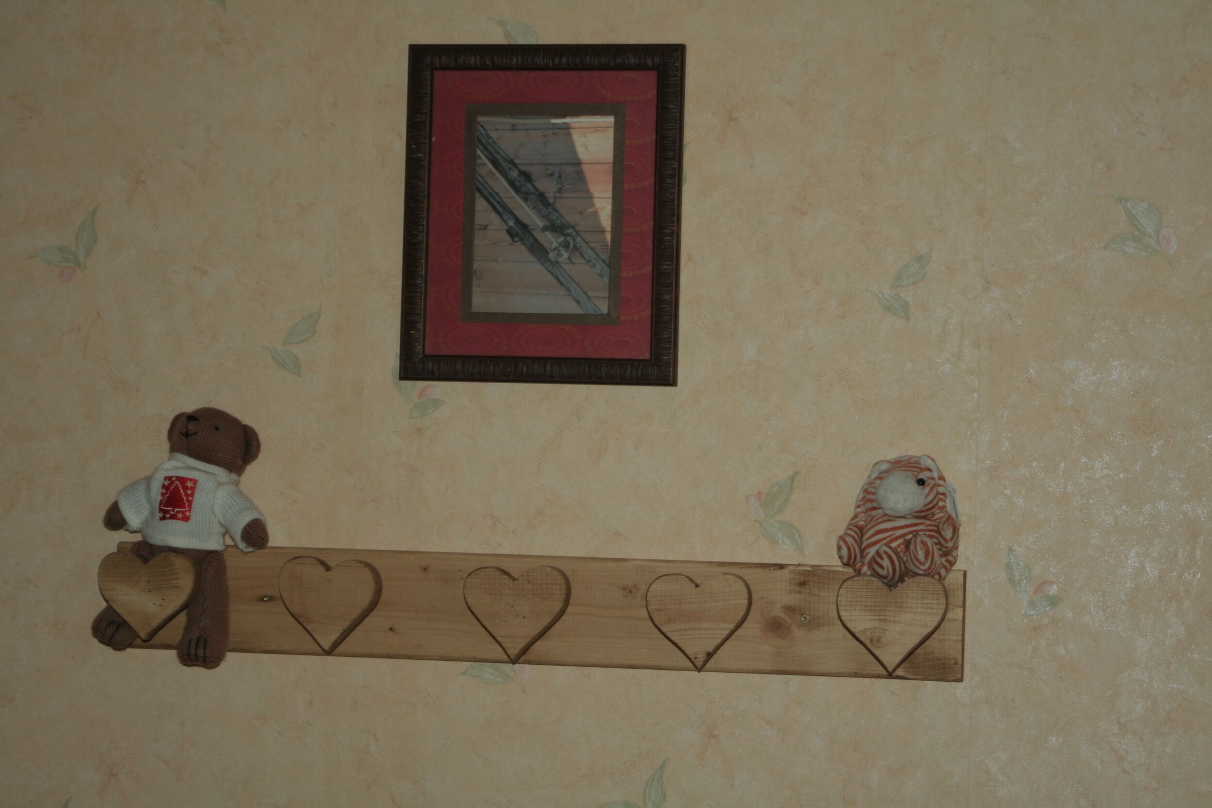 Uno scaffale di legno con fori a forma di cuore e due peluche.