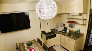 A compact kitchen with a dining area, a flat-screen TV, a microwave, a sink, and a unique ceiling light fixture. - Mifune Central-Bear Shimanouchi No.2 Hotel (Osaka)