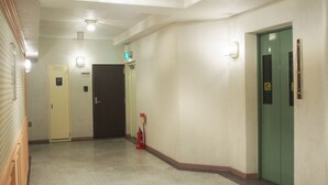 A hallway with a fire extinguisher, a green elevator door, and a white door with a light above it. - Mifune Central-Bear Shimanouchi No.2 Hotel (Osaka)