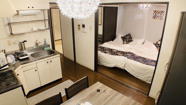 A compact hotel room with a kitchenette, a dining area, and a bed with a patterned bedspread. - Mifune Central-Bear Shimanouchi No.2 Hotel (Osaka)