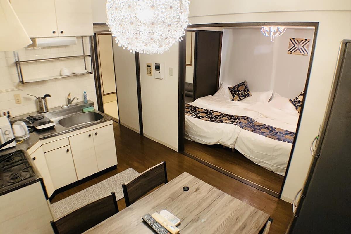 Habitación de hotel compacta con kitchenette, zona de comedor y cama con colcha estampada.