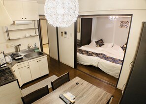 Een compacte hotelkamer met kitchenette, een eethoek en een bed met een decoratief sprei.