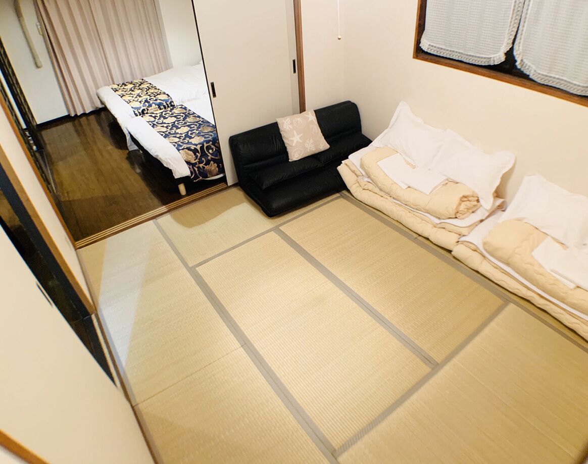 A tatami mat room with a futon bed, a black sofa, and a white sofa.