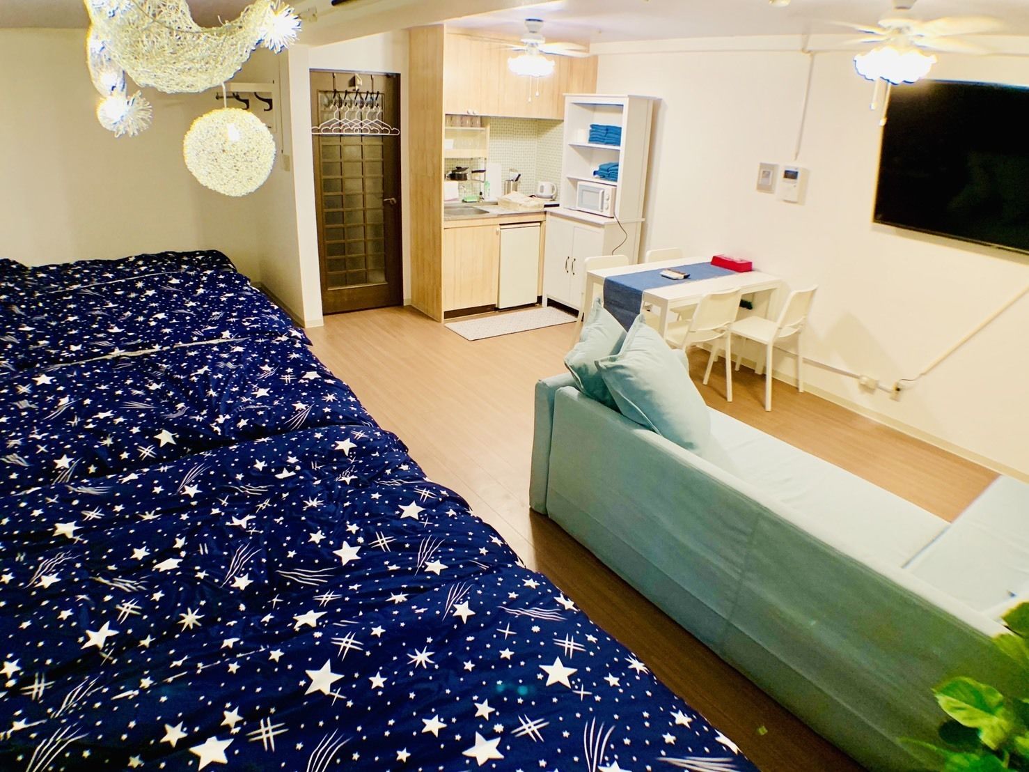 A bedroom with a bed, a sofa, a kitchenette, and a TV.